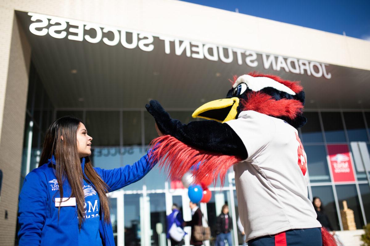 A female student giving a high-five to Rowdy the mascot in front of the JSSB building