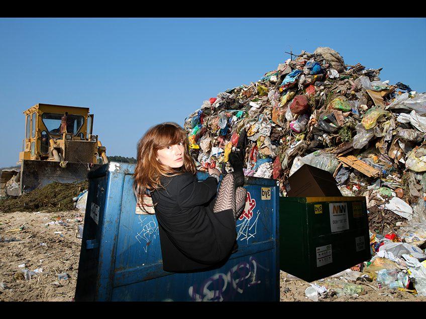 Garbage pile and a woman hanging from a dumpster.